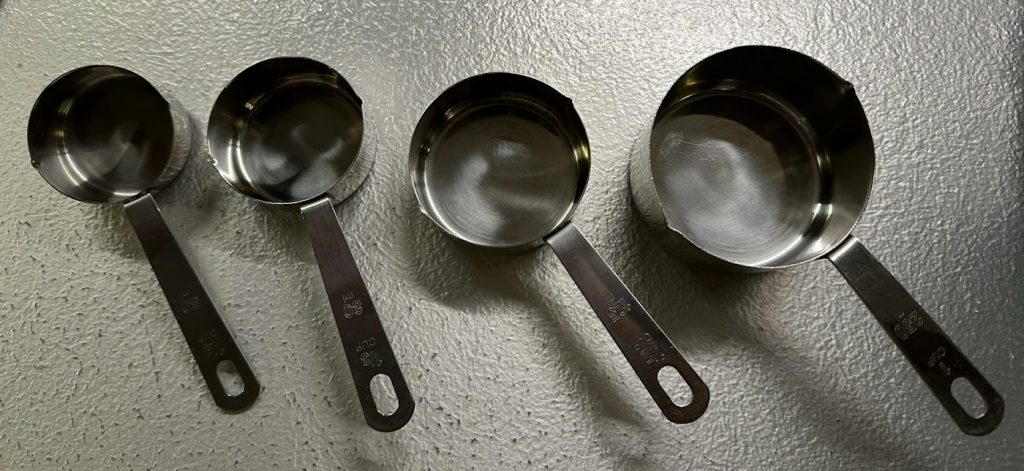 Four stainless steel measuring cups lined up by size on a gray countertop