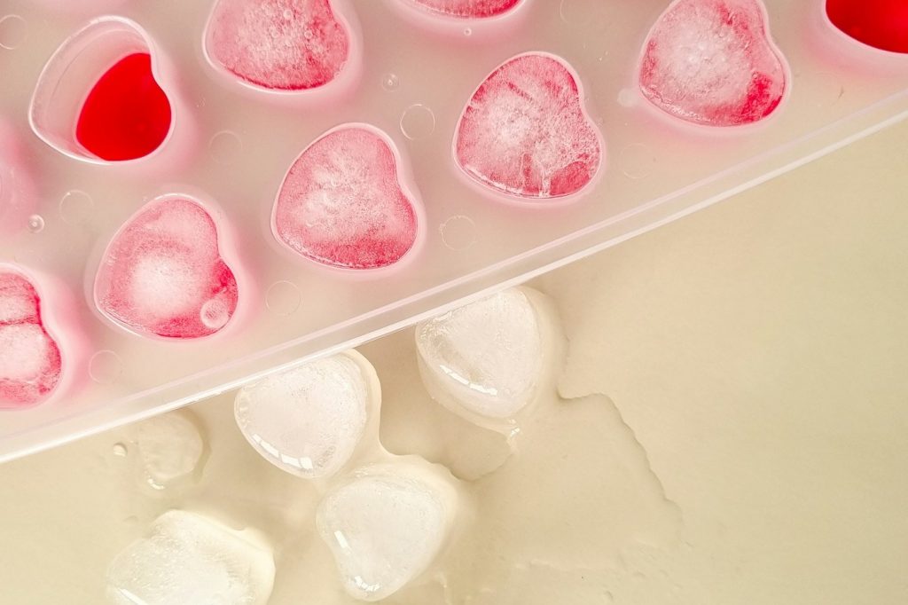 A pink silicone ice tray with heart-shaped cubes being popped out onto a counter