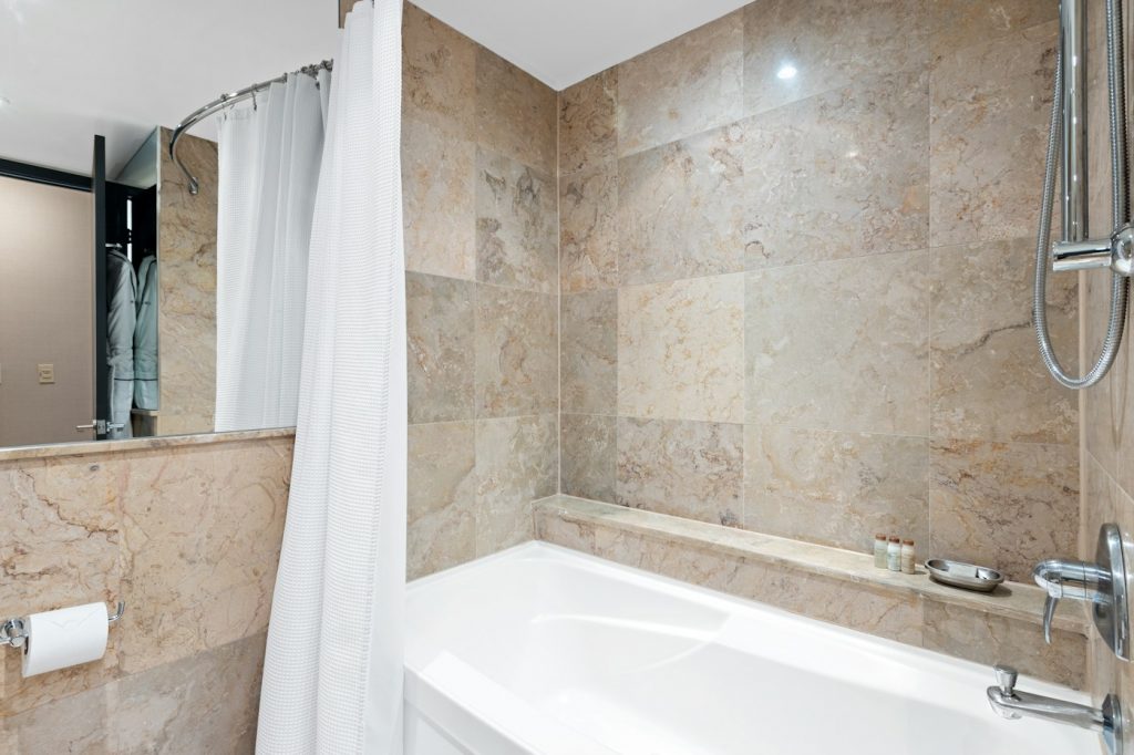 A white shower curtain pulled back beside a tub in a tiled bathroom