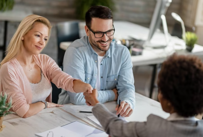 Mid adult couple reaching an agreement with real estate agent in the office women are handshaking
