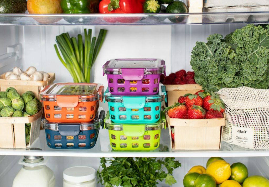 Colorful food storage containers stacked in a refrigerator next to fresh produce