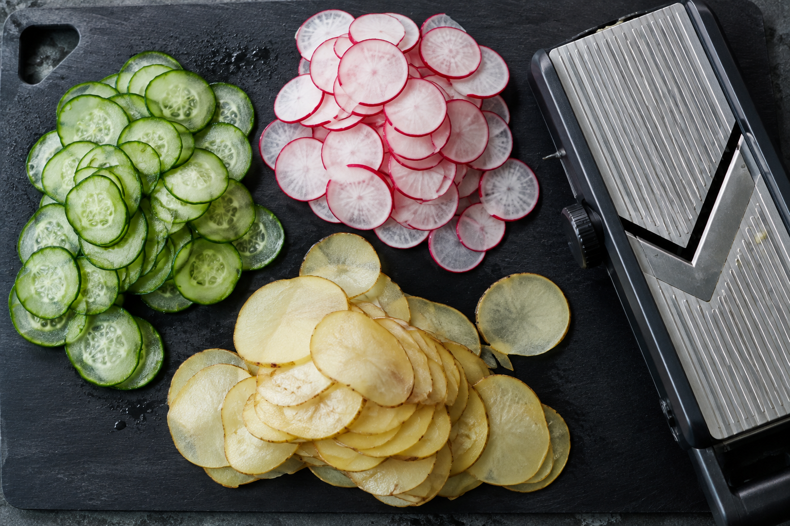 Thin sliced cucumber, radish, and potato beside a mandoline