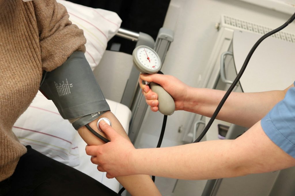 A blood pressure cuff wrapped around a person's bare upper arm while a hand holds the gauge
