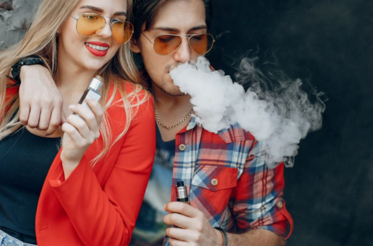 Stylish young couple with vape in a city