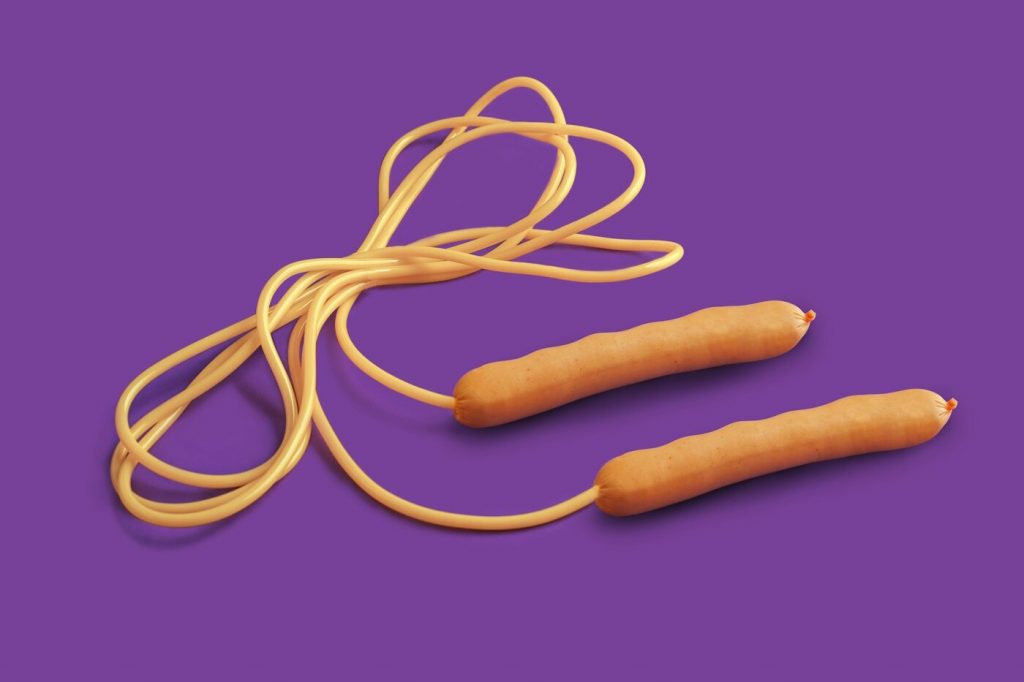 An orange skipping rope with long handles lying coiled on a purple background