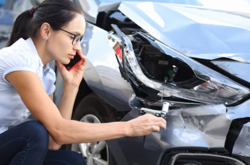 Woman driver is talking on phone next to wrecked car calling insurance agent after car accident