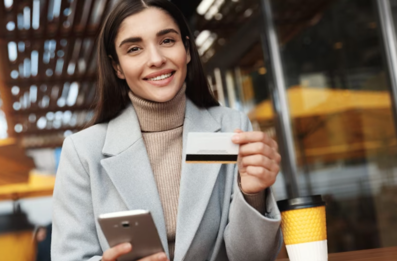 young woman paying online, using credit card and mobile phone while sitting in a coffee shop
