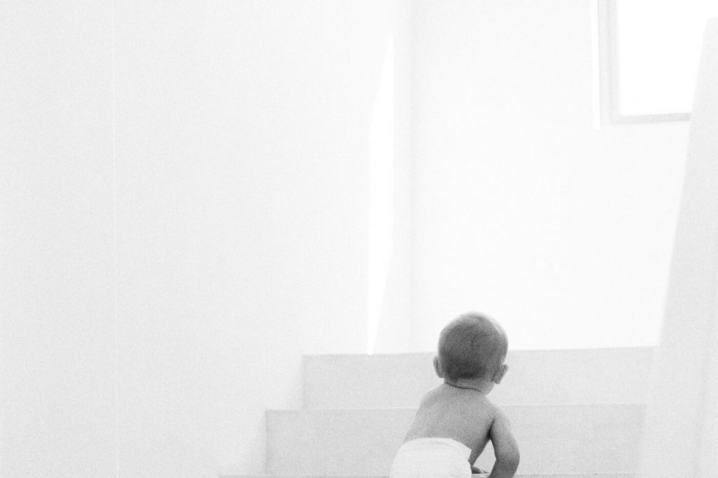 A baby in a diaper climbing a flight of white indoor stairs
