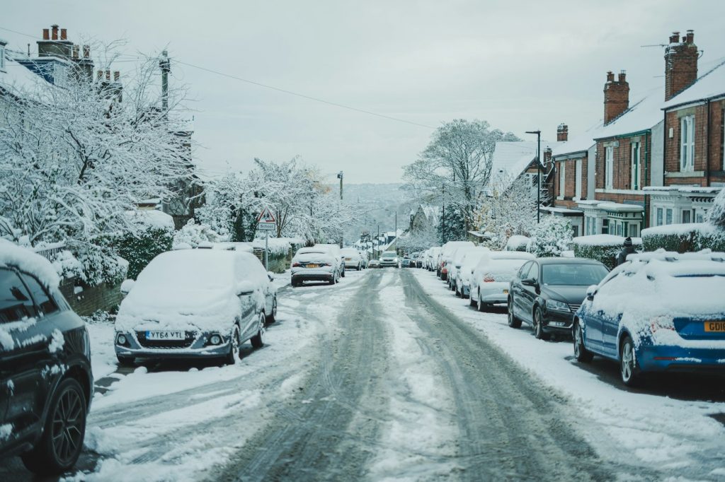 A residential street lined with snow-covered parked cars and houses