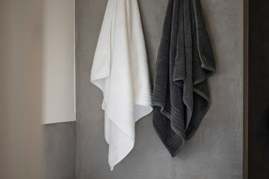 A white towel and a dark gray towel hanging on hooks beside a bathtub
