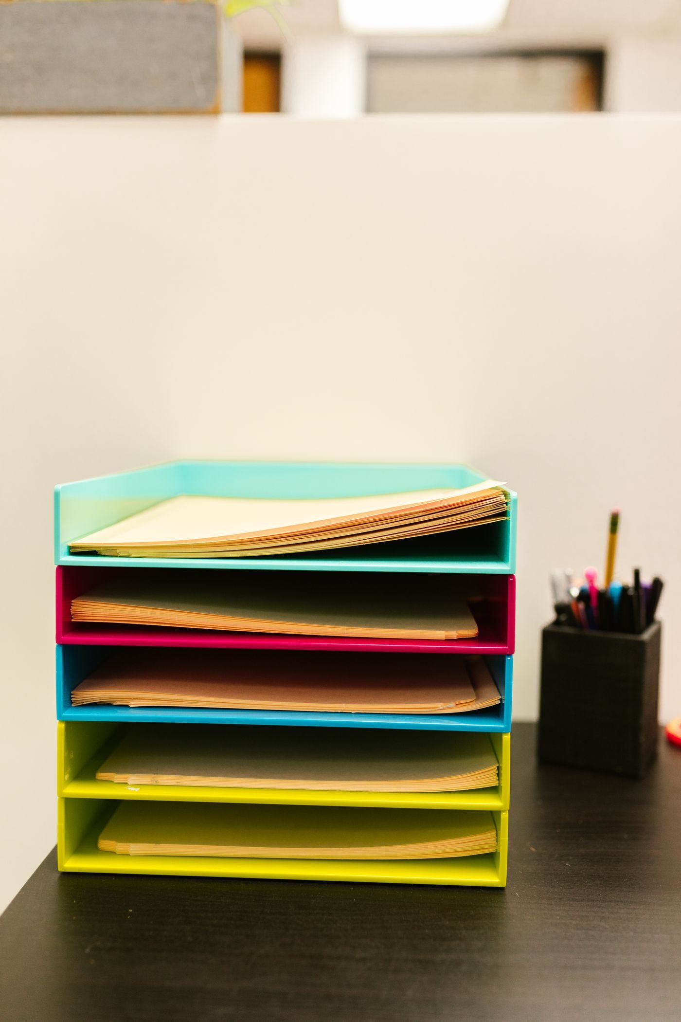 Stock photo of stacked colorful paper trays and a pen cup on a desk, not a listed product