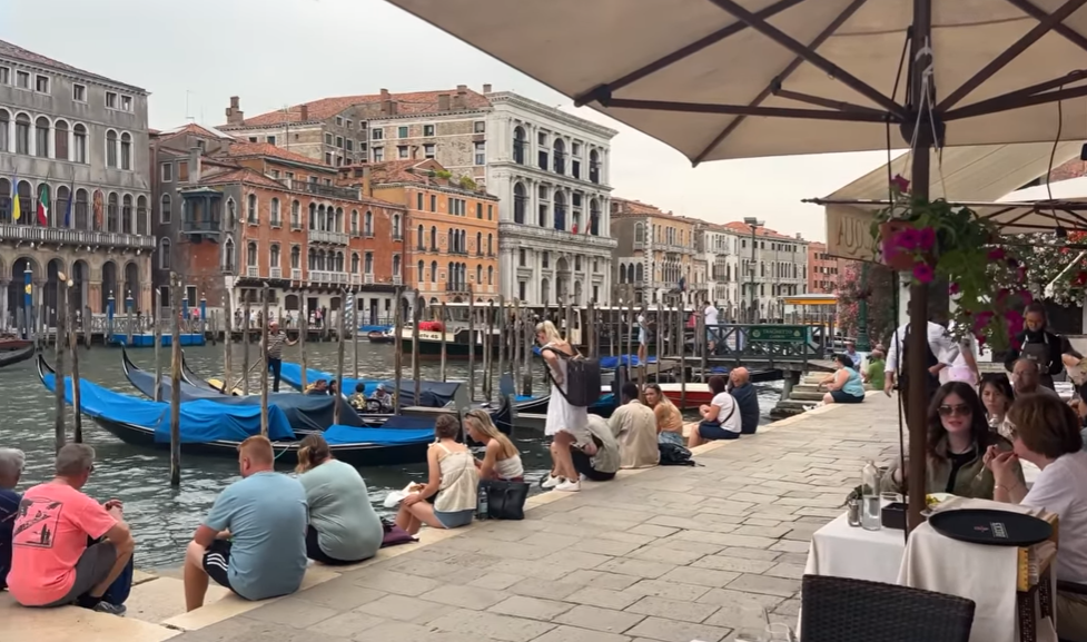 people practicing tourism, sitting on the edge of a river canal.