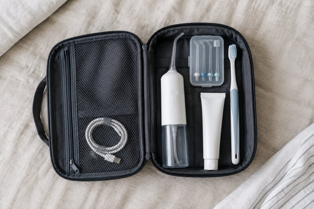 A compact cordless water flosser packed in an open toiletry bag with spare tips and a charging cable