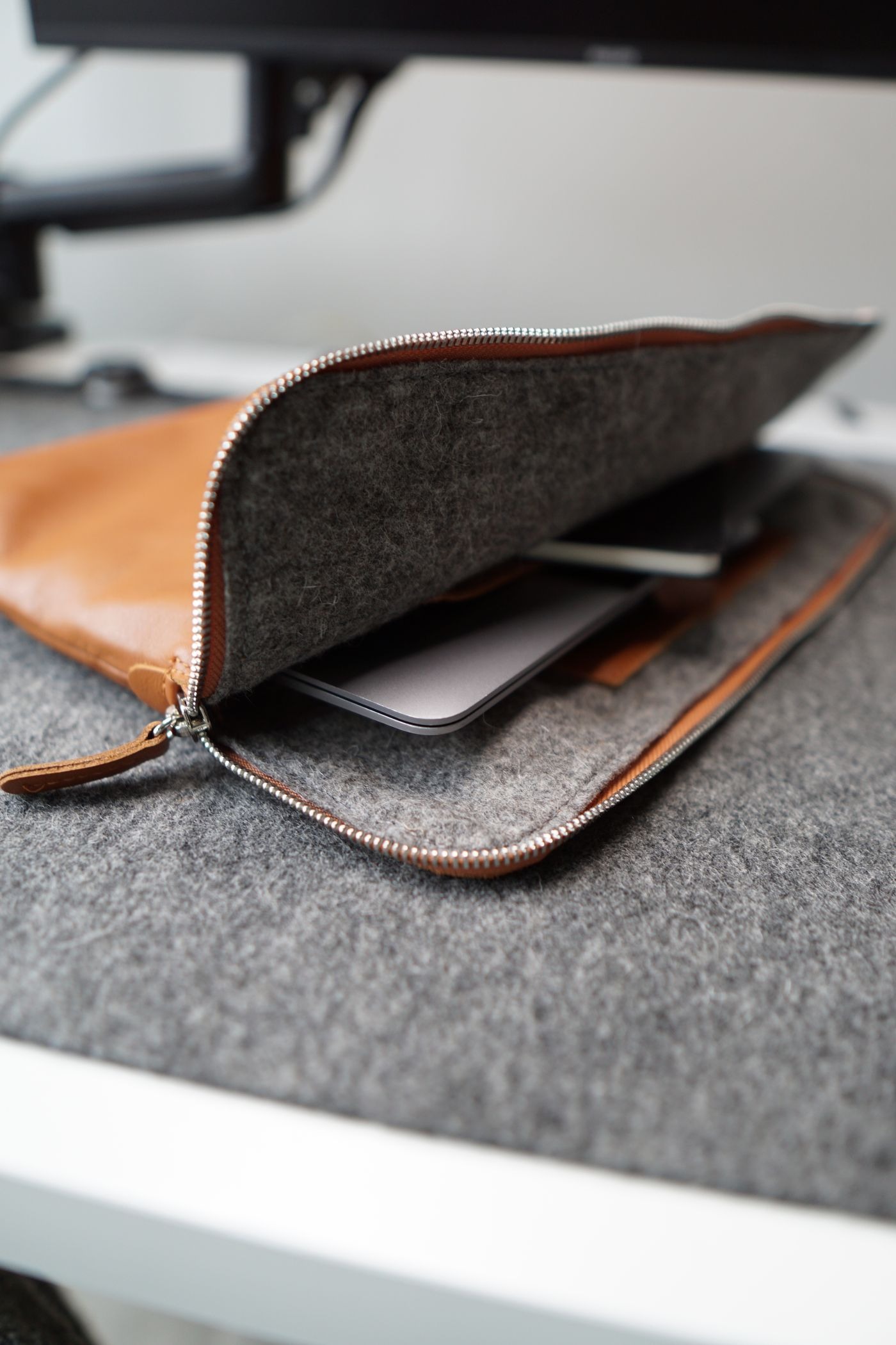 Stock photo of a zippered felt and leather laptop sleeve on a desk, not a listed product