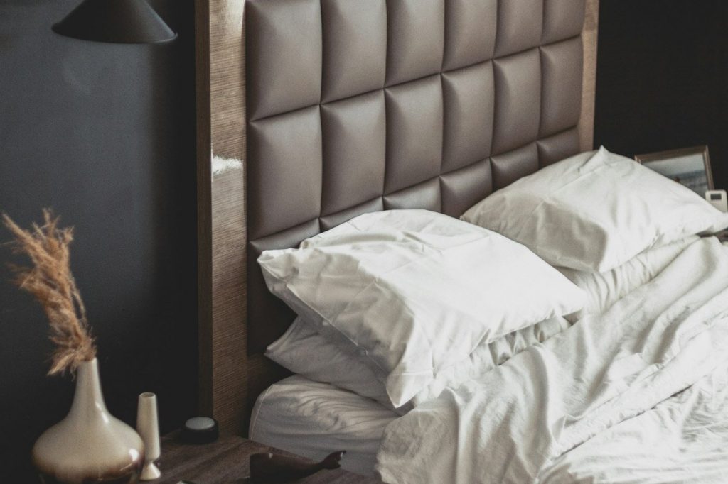 White pillows and rumpled sheets on a bed with a padded headboard next to a small side table