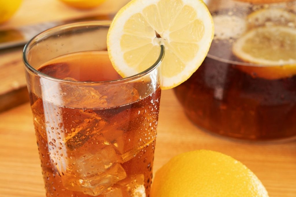 A tall glass of iced tea with ice cubes and a lemon slice on a wooden board