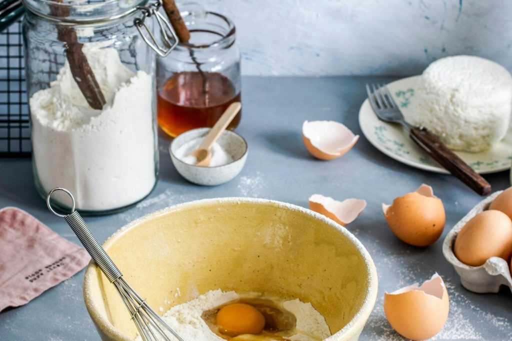 Eggs, flour, and a whisk in a brown mixing bowl on a wooden table
