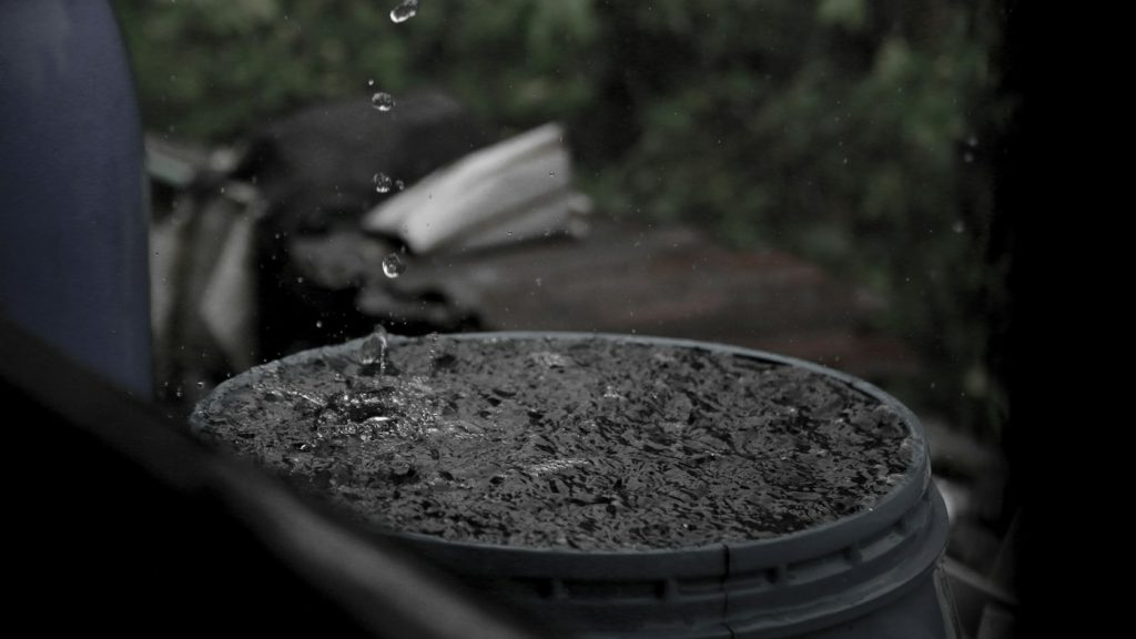 Raindrops falling into a dark plastic barrel filled with water