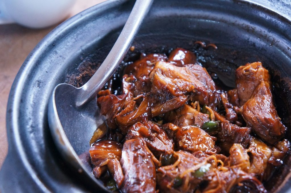 Braised meat in a dark sauce inside a black pot with a serving spoon