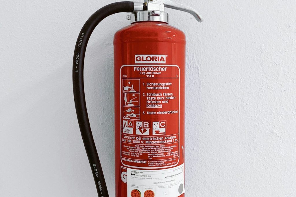 A red dry-powder fire extinguisher with a black hose hanging on a white wall