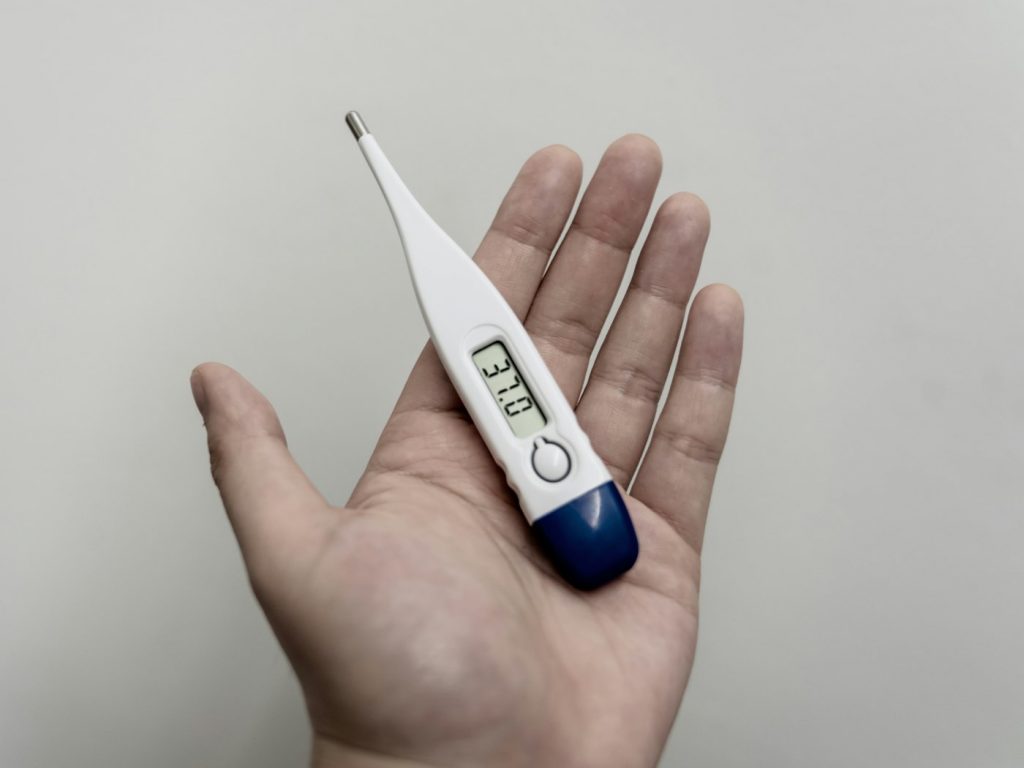 A white and blue digital stick thermometer resting in an open palm