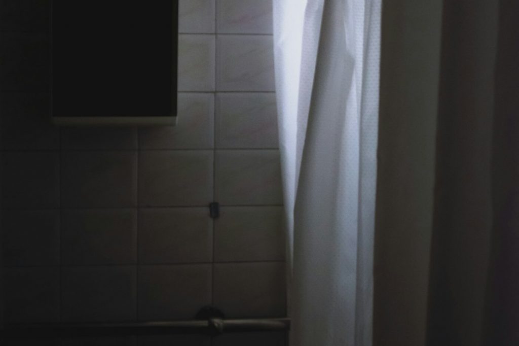 A white shower curtain hanging from metal rings on a rod against a tiled wall