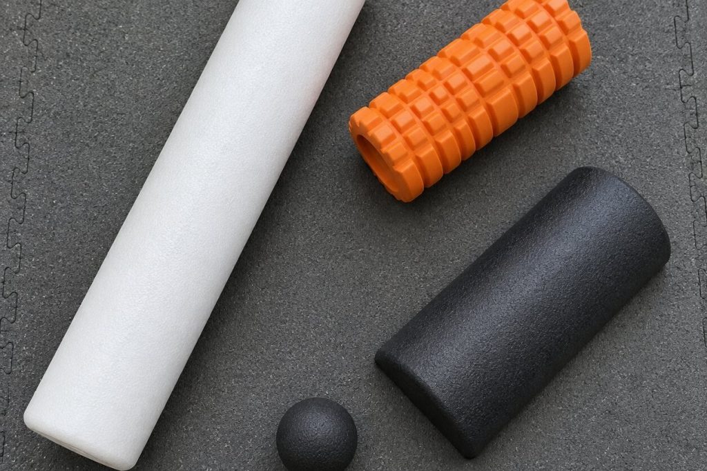 Three foam rollers of different sizes and textures and a massage ball on a gray gym mat