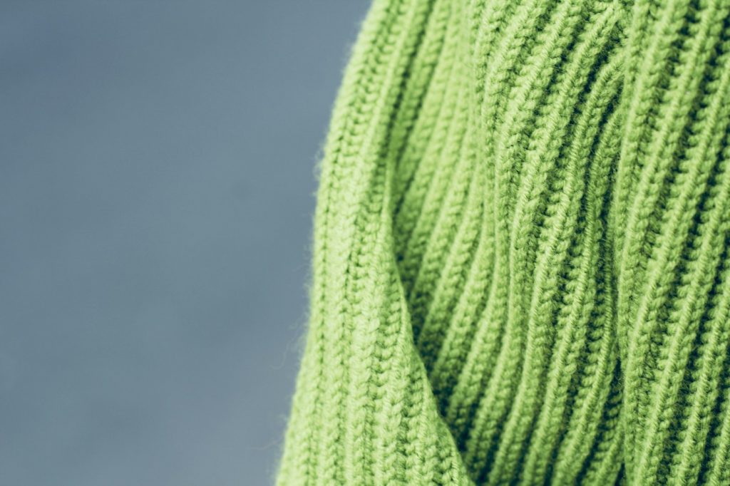 Close-up of a green ribbed knit sweater against a gray background