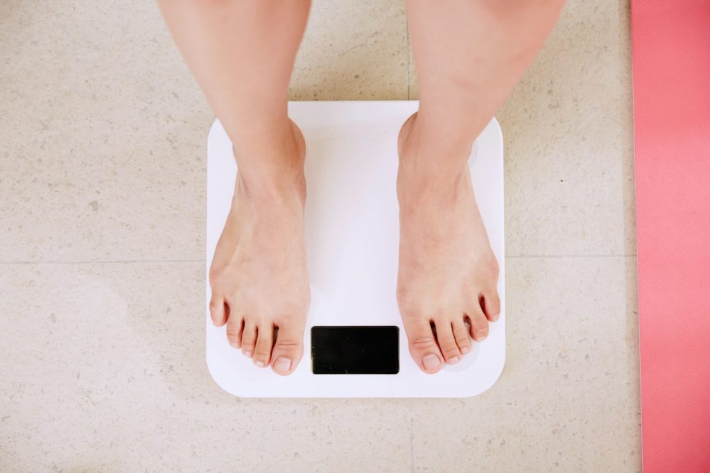 Person standing barefoot on a white digital bathroom scale on a tile floor