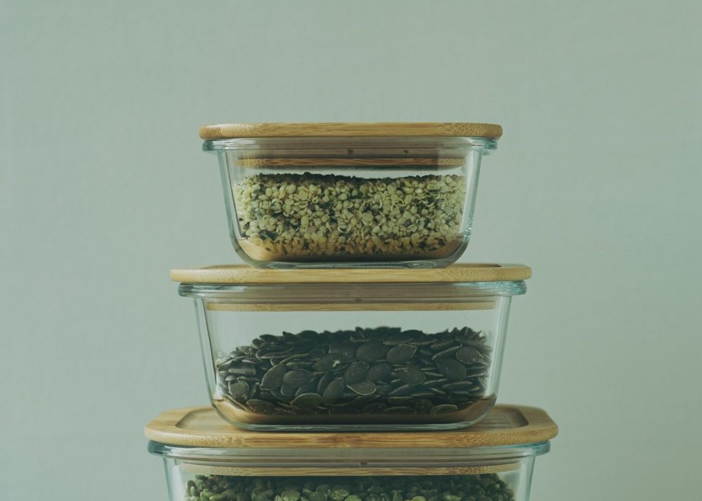 Three glass food storage containers with wooden lids stacked on a table