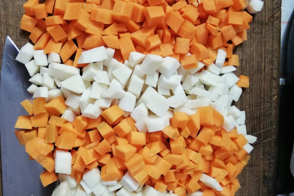 Neat piles of diced carrot and white onion on a dark wooden board