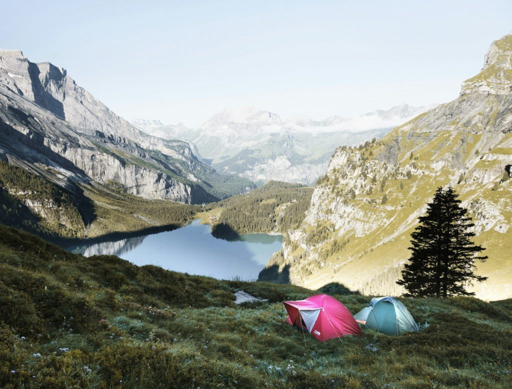 Two small tents pitched on a grassy slope above a mountain lake