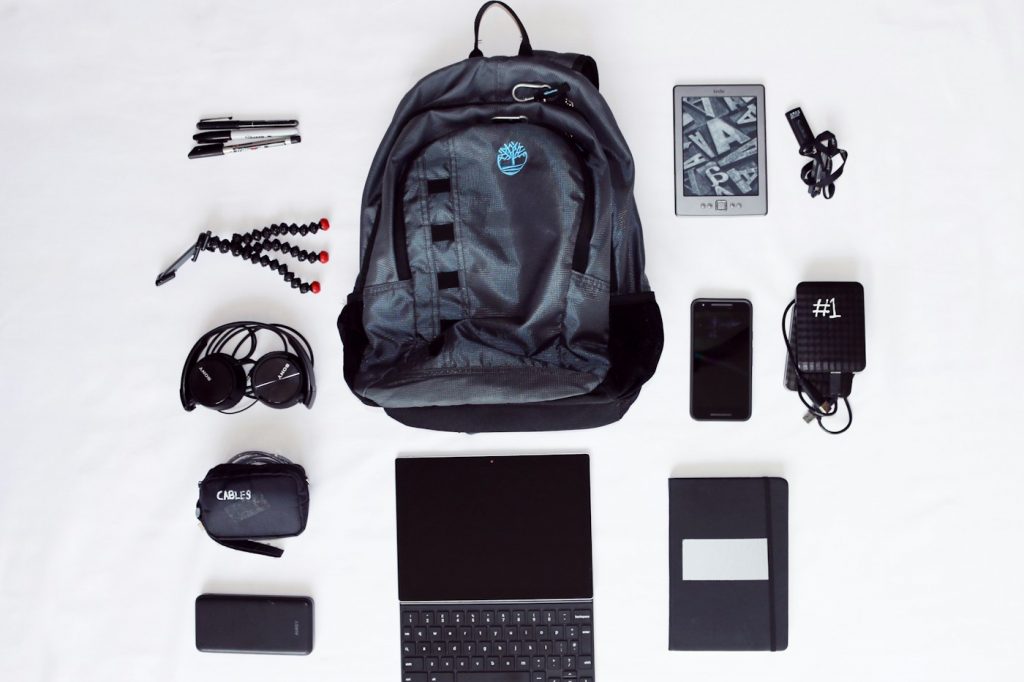 A backpack with work and travel essentials laid out around it