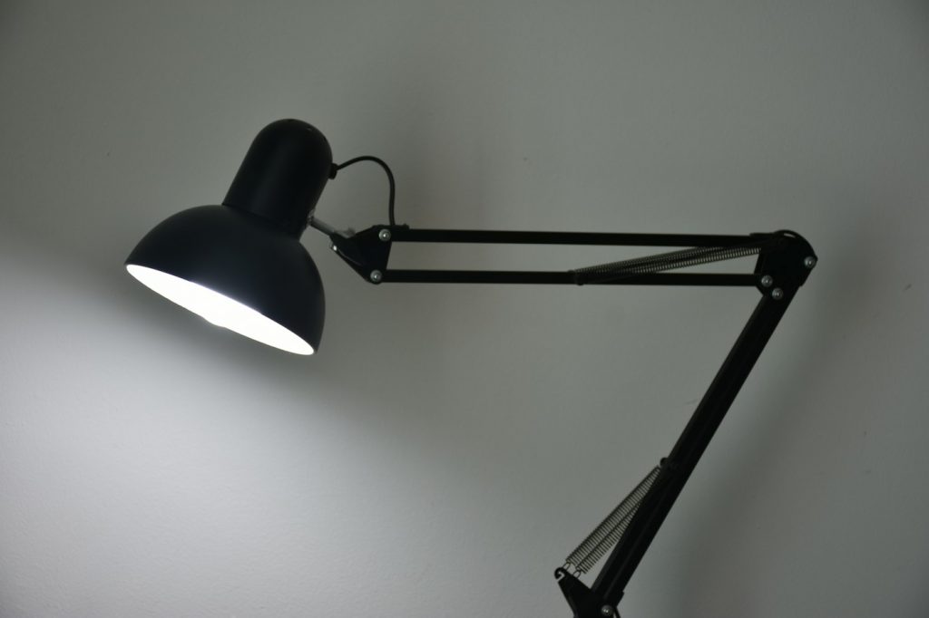A black swing-arm desk lamp with a round shade shining against a light gray wall
